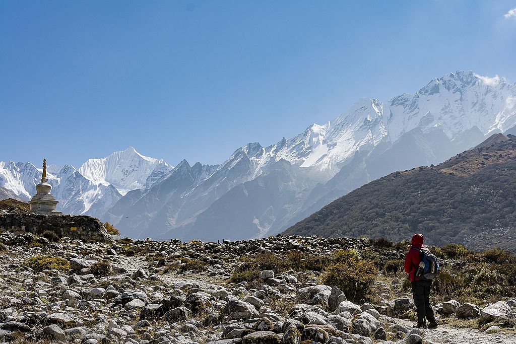 A traveler taking a short break during her trek to Kyanjin Gompa in the Langtang National Park to admire the Langtang Mountain range